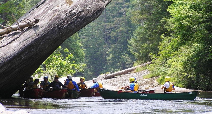 students sitting in canoes pause for a break in the shade of a large rock